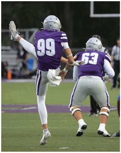 Three people in football uniforms are on a field with one person kicking a ball while two others prepare to block or defend. Description generated by AI