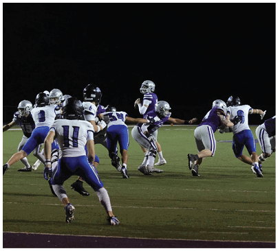 Two people wearing athletic clothing and cleats are running on a sports field with artificial turf. Description generated by AI