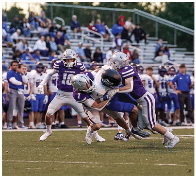 People wearing athletic gear are engaged in a close physical struggle on a grassy field, likely during a sports game. Description generated by AI