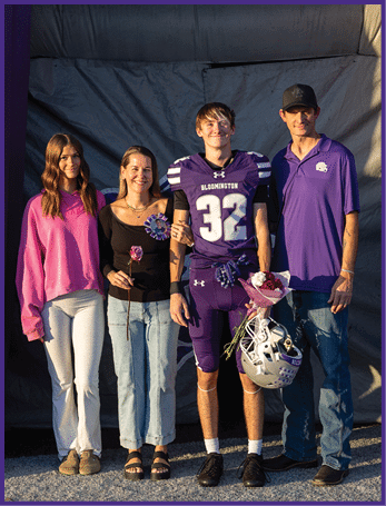 Three people stand smiling next to a large purple inflatable structure with the word “PANTHERS" written vertically in white and purple letters. Description generated by AI