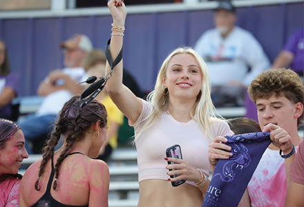 Several people with braided hair and paint on their skin are gathered outdoors, one holding a phone and another holding a blue cloth with a panther design. Description generated by AI
