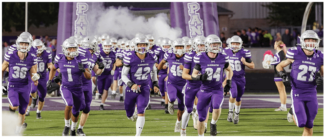 A group of people wearing purple sports uniforms and helmets are running out of a smoke-filled inflatable tunnel with the word “SOUTH" displayed above. Description generated by AI