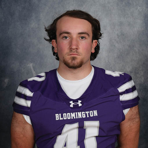 A person with medium-length hair wearing a purple sports jersey with the word Bloomington and the number 41 stands against a gray textured background. Description generated by AI