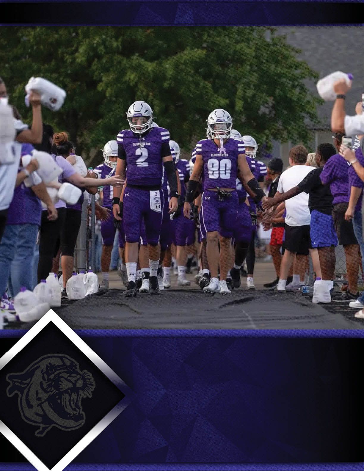 Two people in purple football uniforms walk down a pathway lined with people on both sides who are reaching out to them. Description generated by AI