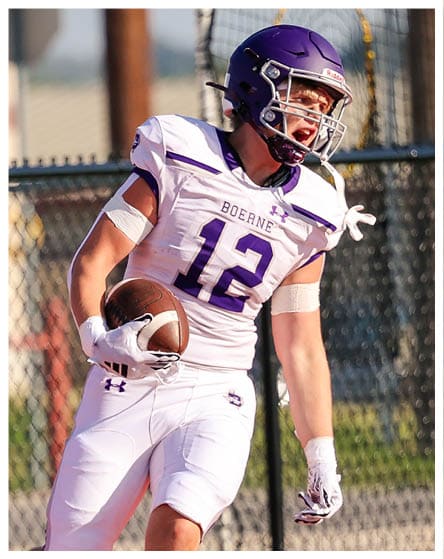 A person wearing a white football uniform with the number 12 is running on a field while holding a football near the end zone. Description generated by AI