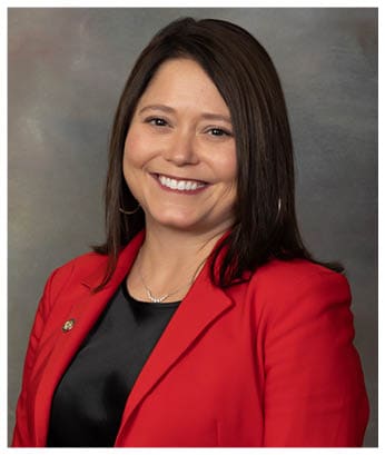 A person wearing a red blazer and a silver necklace is smiling with visible teeth. Description generated by AI