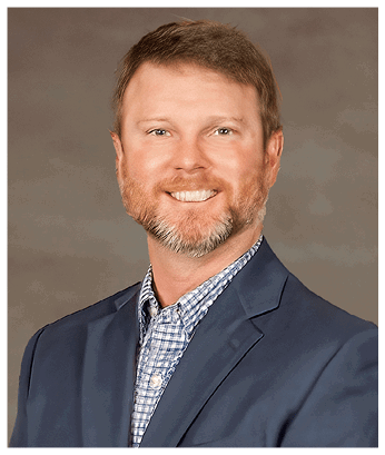 A person wearing a blue blazer over a blue and white checkered shirt is smiling. Description generated by AI