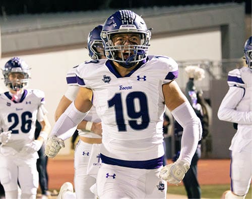 A person wearing a football uniform and helmet with the number 19 is shouting or expressing excitement on a sports field. Description generated by AI