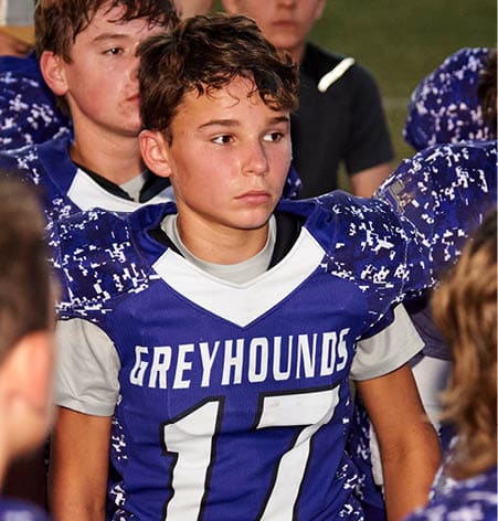 A person wearing a blue sports jersey with the word “GREYHOUNDS" printed in white across the chest. Description generated by AI