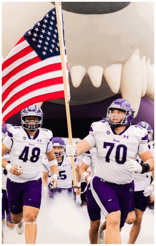 People wearing purple sports uniforms are running through smoke or fog on a field. Description generated by AI