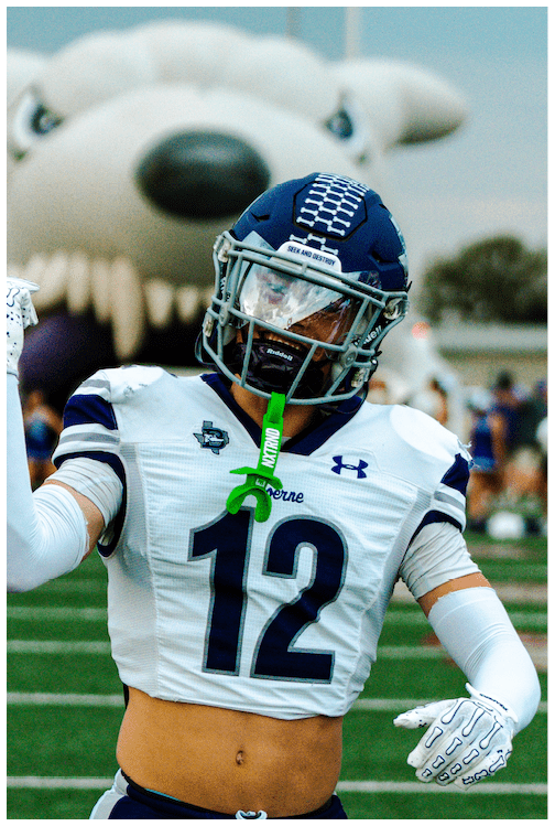 A person wearing a football uniform with the number 12 and a helmet is on a field with a large inflatable wolf head in the background. Description generated by AI