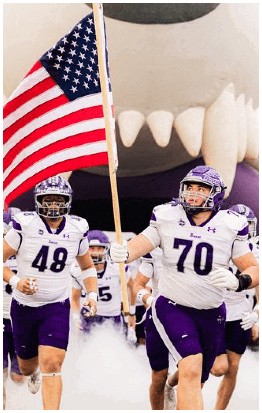 People wearing purple sports uniforms are running through smoke or fog on a field. Description generated by AI