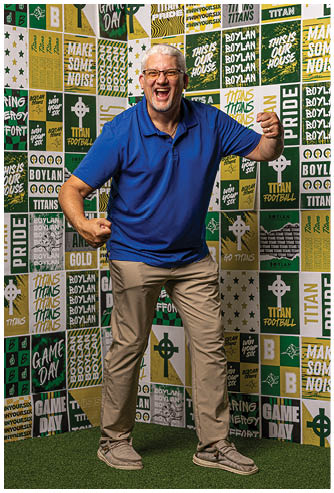A senior person with white hair and glasses is laughing joyfully while wearing a blue polo shirt in front of a colorful background with motivational text. Description generated by AI