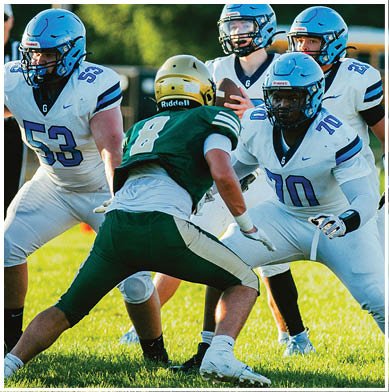 Four people in football uniforms are engaged in a play on a grassy field with one person in a green uniform facing three others in white uniforms. Description generated by AI