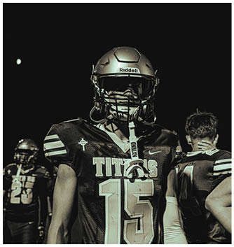 A person wearing a silver Riddell football helmet with a dark background. Description generated by AI