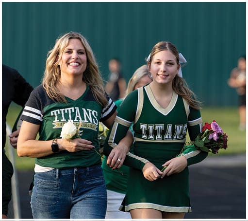 A person wearing a green cheerleading uniform with the word Titans is holding a bouquet of flowers and smiling while standing outdoors. Description generated by AI