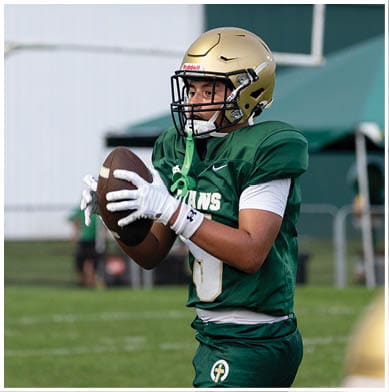 A person wearing a green football jersey and gold helmet is catching a football on a grassy field. Description generated by AI