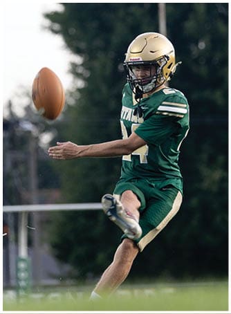 A person wearing a green football jersey and a gold helmet is standing outdoors with a blurred background. Description generated by AI