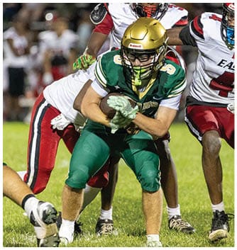 A person wearing a red and white football uniform with the word East and the number 4 is running on a grassy field during a game. Description generated by AI
