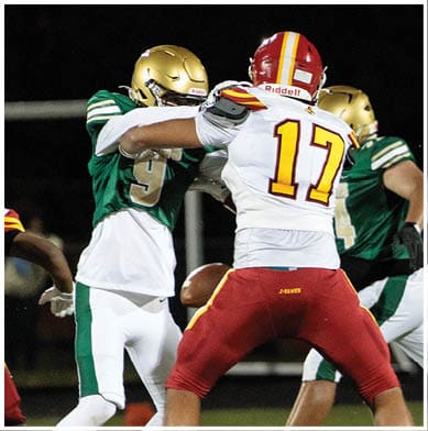 Two people in football uniforms are engaged in a play on a field at night, with one wearing a white and red uniform and the other in green and white. Description generated by AI