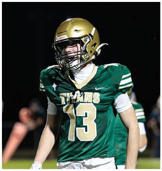 A person wearing a green football jersey with the number 13 and a gold helmet is standing on a field at night. Description generated by AI