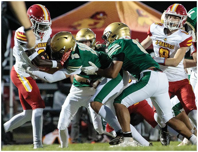 Several people wearing football uniforms are engaged in a play on a grassy field during a nighttime game. Description generated by AI