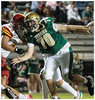 Two football players in helmets and uniforms are engaged in a close physical play on a field with blurred spectators in the background. Description generated by AI