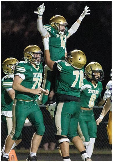 People wearing green and gold football uniforms celebrating on a field at night. Description generated by AI