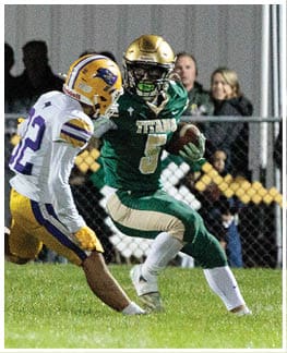 Two people in football uniforms are actively engaged in a play on a grassy field, with one person in green running with the ball and the other in white and yellow attempting to tackle. Description generated by AI