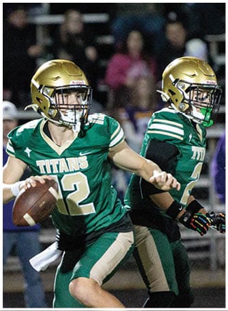 A person wearing a green football uniform and gold helmet is running on a field with another person partially visible beside them. Description generated by AI