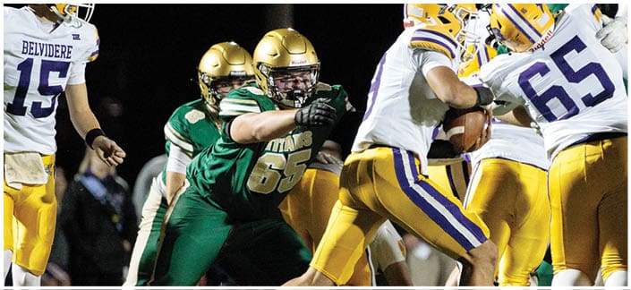 People in football uniforms are engaged in a play on a field at night with some players blocking and others attempting to tackle. Description generated by AI