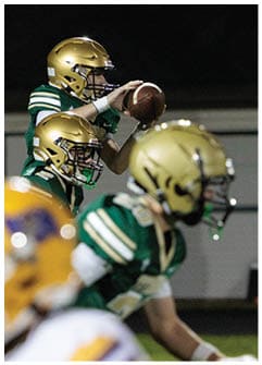 Two people in football uniforms and helmets are engaged in a play, with one holding a football ready to throw. Description generated by AI