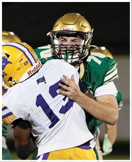 Two people in football uniforms and helmets are engaged in a physical play during a game, with one person wearing a white jersey and the other in a green jersey. Description generated by AI