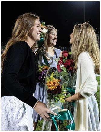 People dressed in formal and casual clothing are smiling and holding bouquets of flowers on a grassy field at night. Description generated by AI