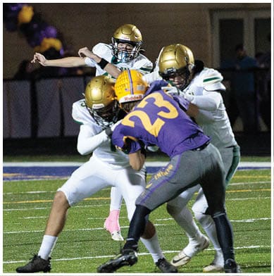 A group of people wearing football helmets and uniforms are engaged in a play on a football field under stadium lights. Description generated by AI