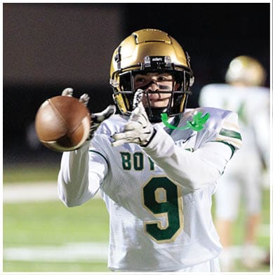 A person wearing a white and green football uniform with the number nine is reaching out to catch a football on a field at night. Description generated by AI