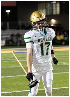 A person wearing a gold football helmet and white jersey is partially visible against a dark background. Description generated by AI