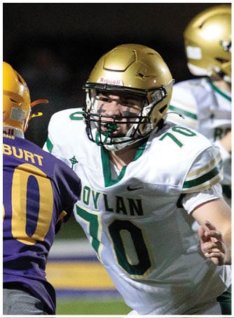 Two people in football uniforms are engaged in a play on the field with one person preparing to throw the ball and the other attempting to block. Description generated by AI