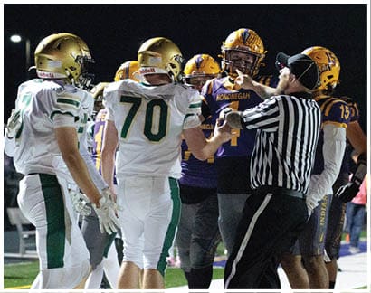 A group of football players from two teams and a referee are interacting on the field during a game at night. Description generated by AI