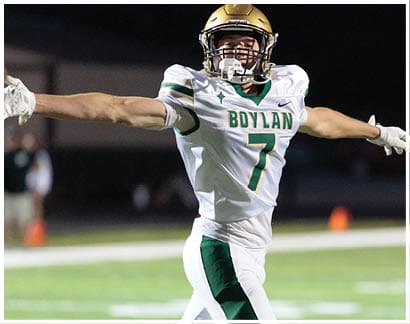 A person wearing a football uniform with the name “Boylan" and number 7 is celebrating with arms outstretched on a football field at night. Description generated by AI