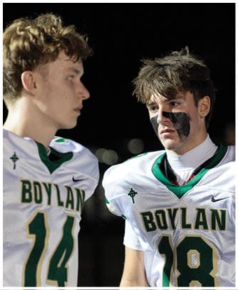 Two people wearing football uniforms with “BOYLAN" on the front are standing close to each other, one with black face paint under the eyes. Description generated by AI