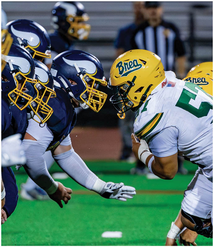 Three football players in blue and white uniforms running on a field. Description generated by AI