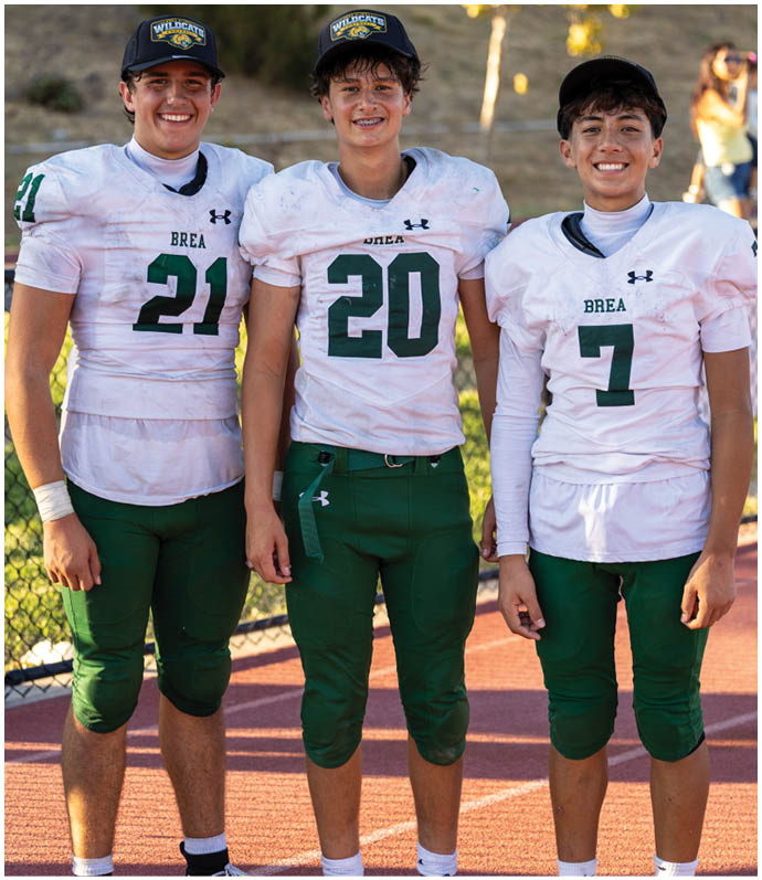 Three football players in blue and white uniforms running on a field. Description generated by AI