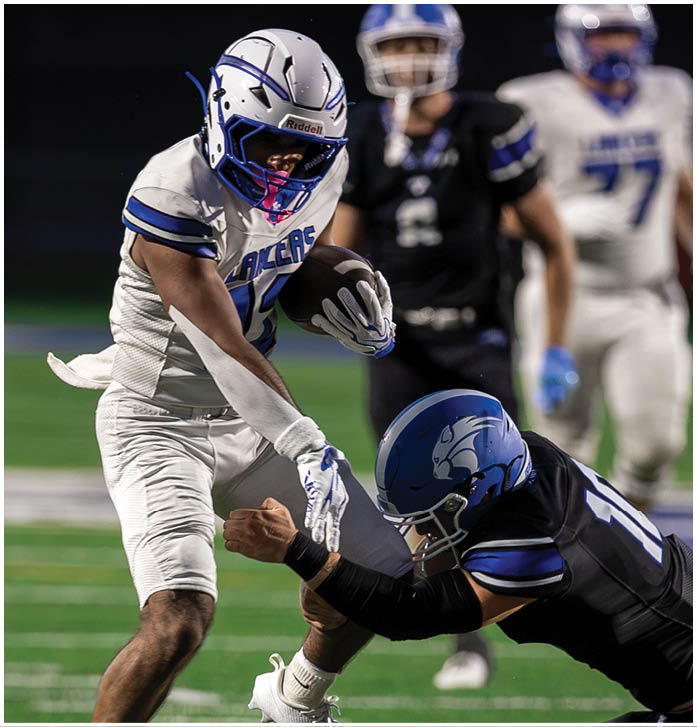 A person in a white football uniform is running with the ball while another person in a black uniform is attempting to tackle them on a football field. Description generated by AI