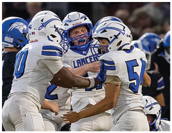 People in football uniforms are celebrating on the field during a game with a crowd in the background. Description generated by AI