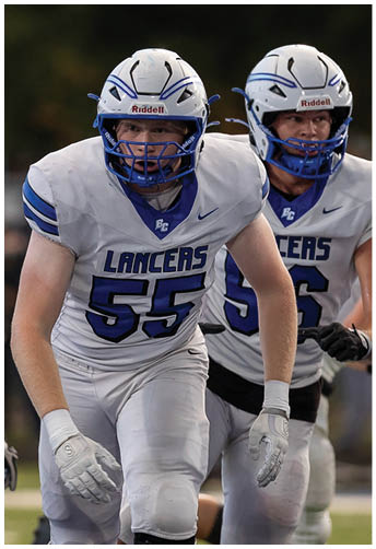 A person wearing a white football uniform with the number 55 and a helmet is running on a field during a game. Description generated by AI