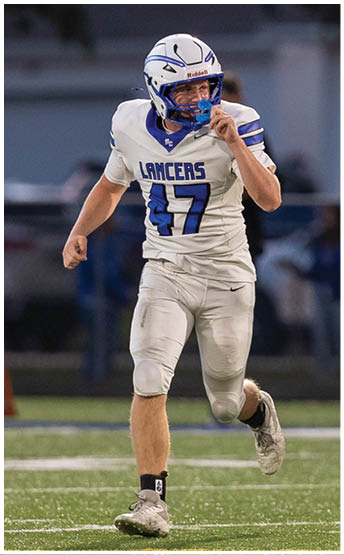A person wearing a white football uniform with the number 47 and a helmet is running on a field during a game. Description generated by AI