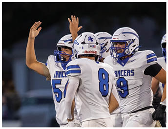 A group of people wearing white football uniforms with blue helmets and the word “Lancers" are celebrating on a football field. Description generated by AI