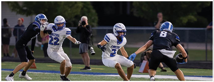 Four people in football uniforms are actively engaged on a field with one person holding the ball and others preparing to block or tackle. Description generated by AI
