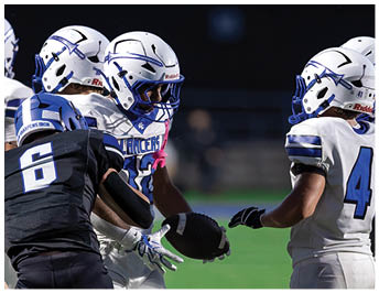 People wearing football uniforms in black and white are gathered on a field during a game, with one person holding a football. Description generated by AI